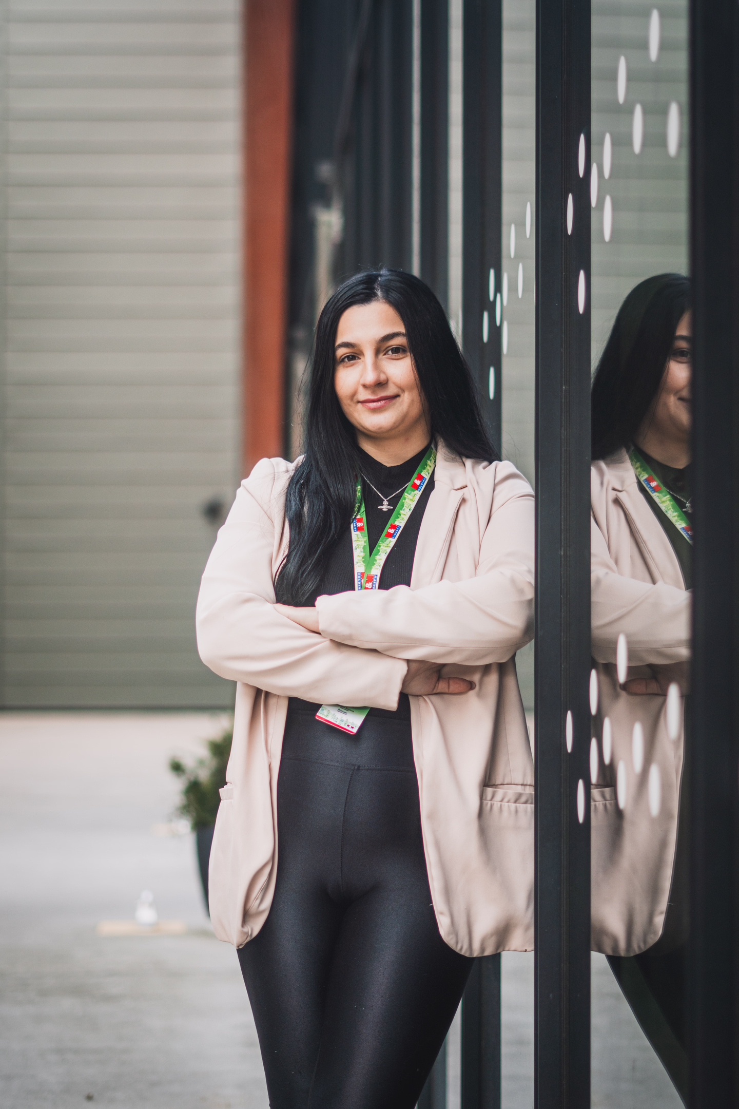 Moderní firemní portrét ženy s dlouhými černými vlasy, focený u prosklené fasády kancelářské budovy.