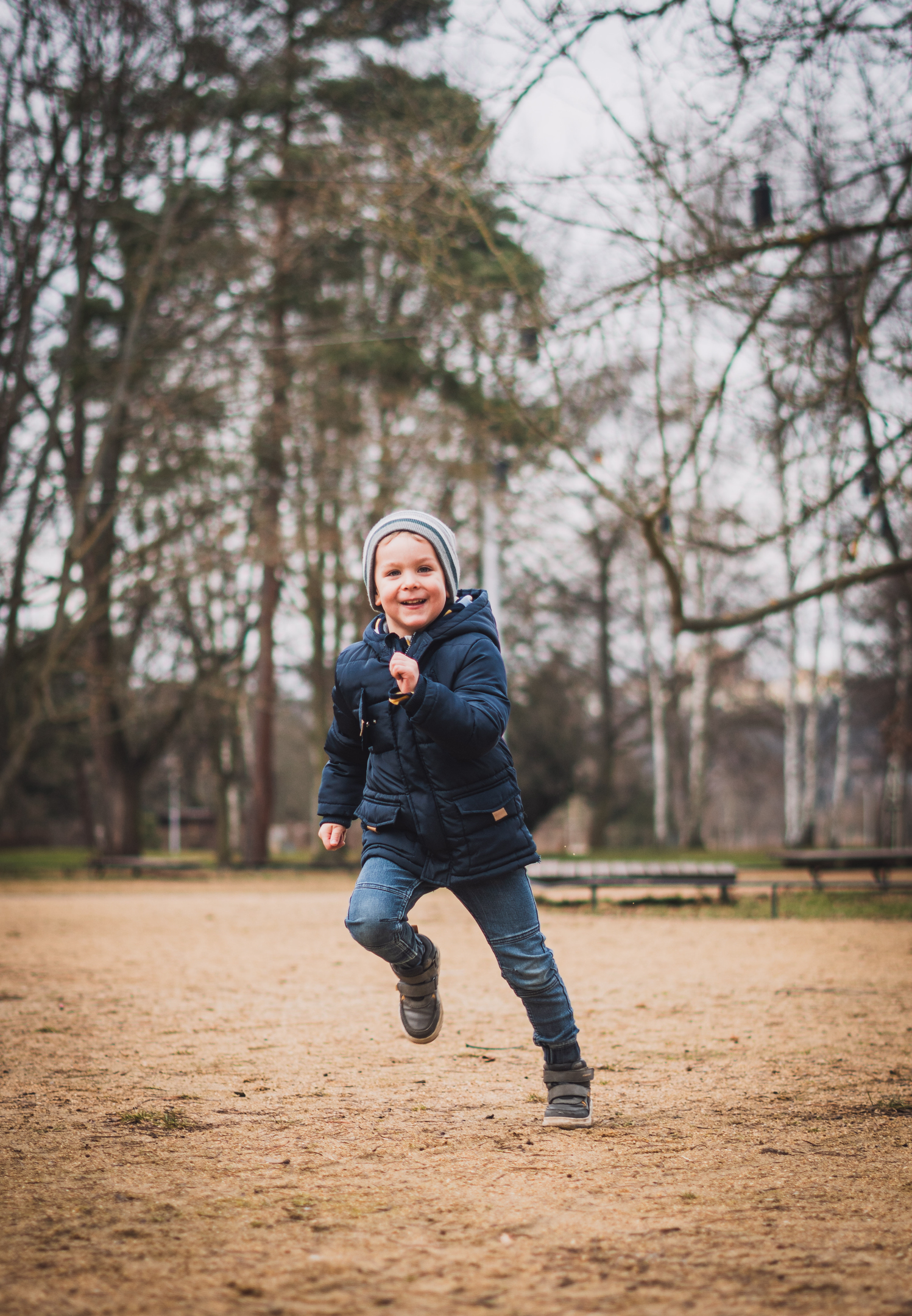 Akční fotografie usměvavého chlapce, který s radostí běží směrem k fotografovi v parku.